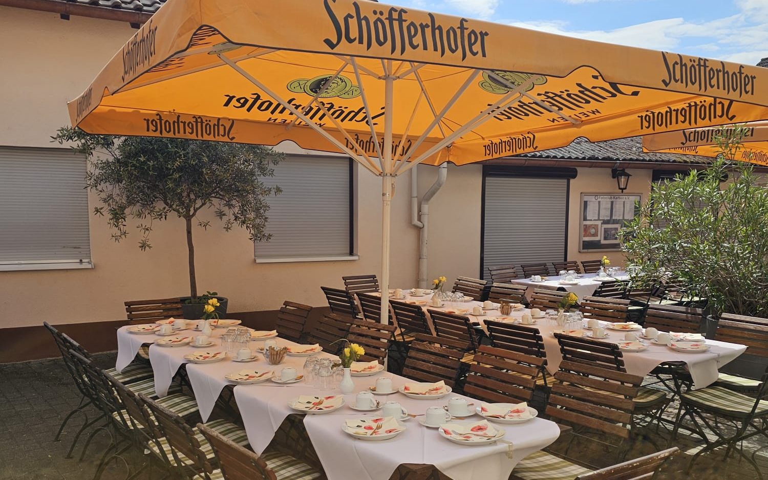 Lange, eingedeckte Tafel im Biergarten unter orangefarbenen Sonnenschirmen